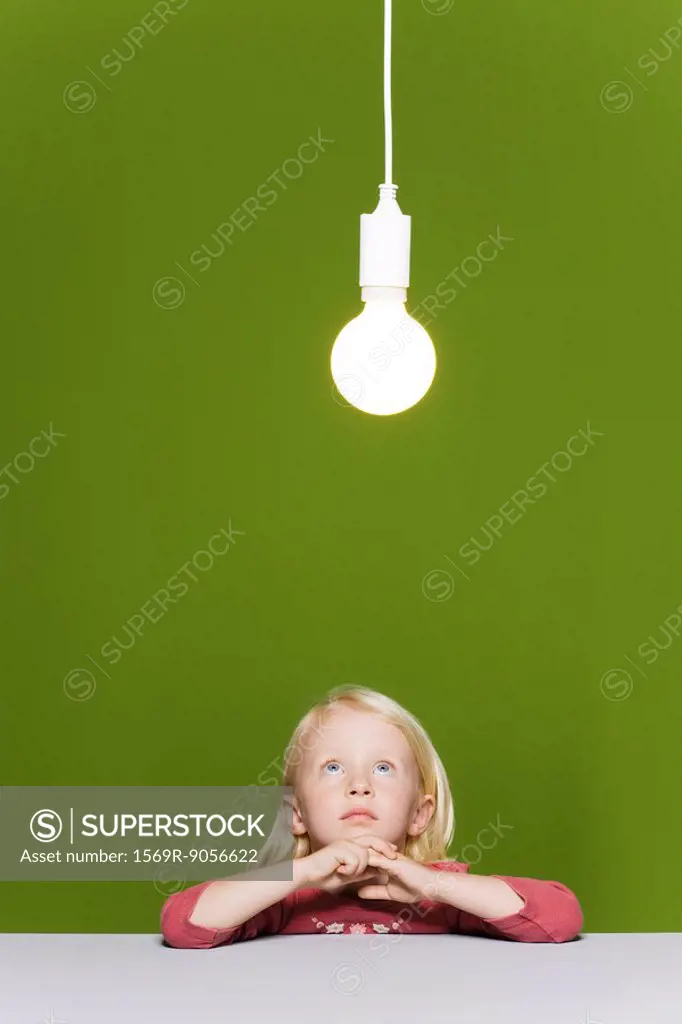 Little girl contemplating illuminated light bulb suspended overhead