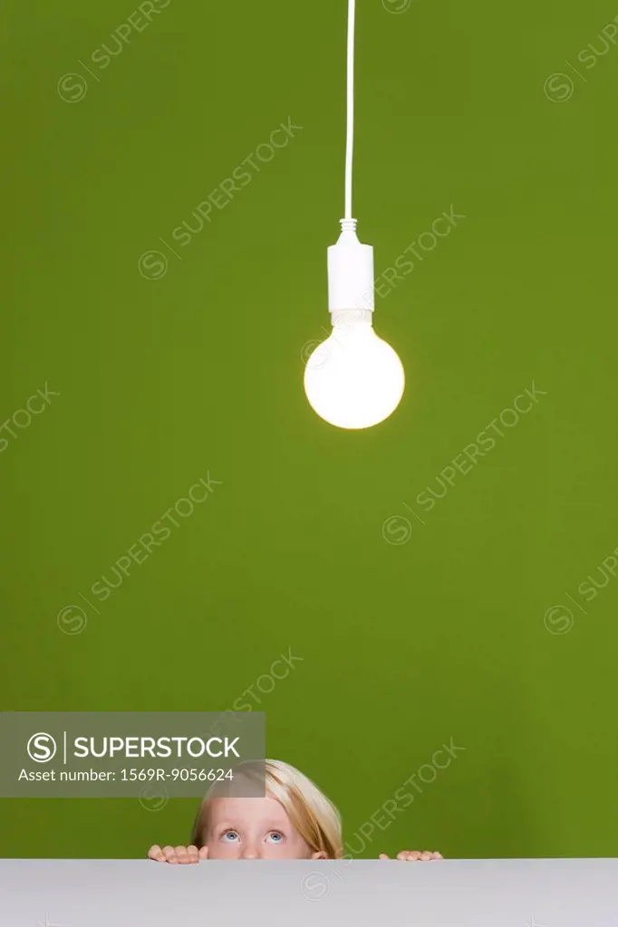 Little girl looking fearfully up at illuminated light bulb suspended overhead