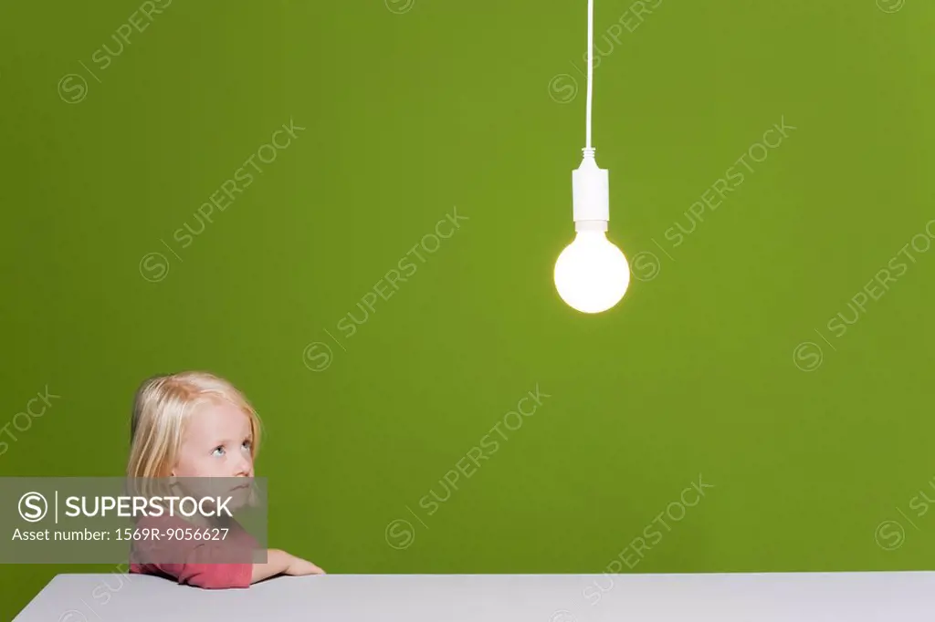 Little girl biting lip looking with concern up at illuminated light bulb suspended overhead