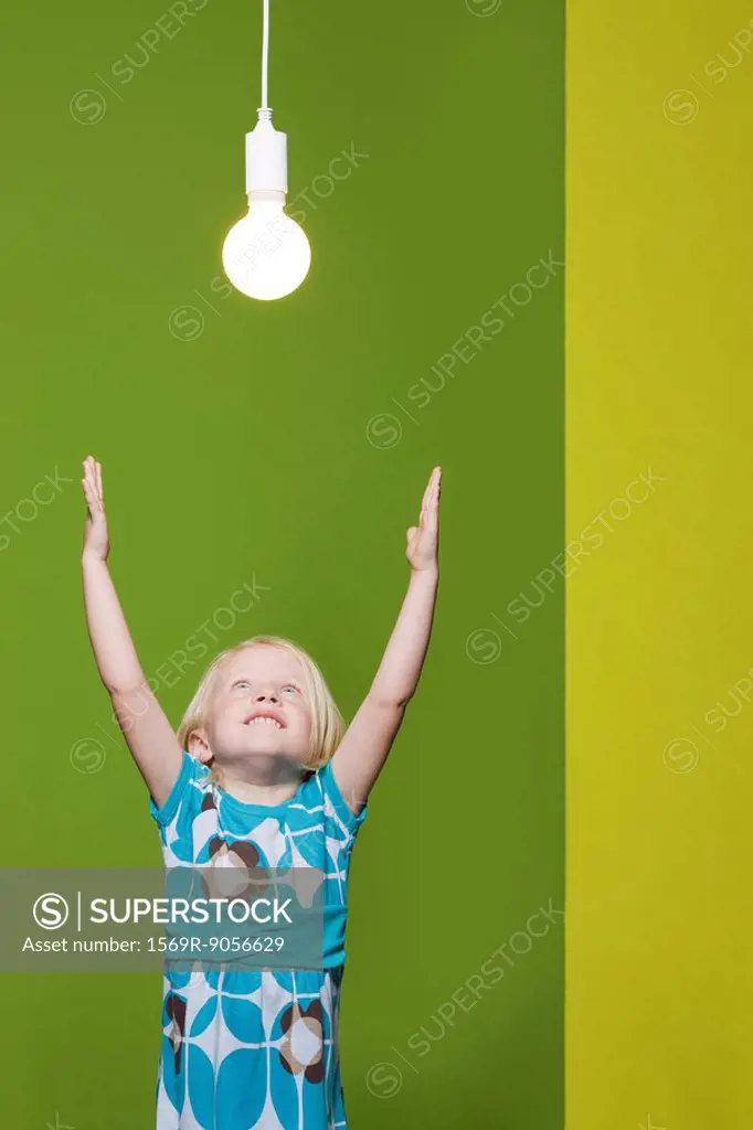 Little girl with arms raised, reaching for light bulb suspended overhead