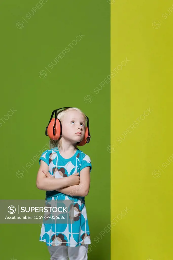 Little girl with arms folded, wearing protective headphones, defiantly looking away