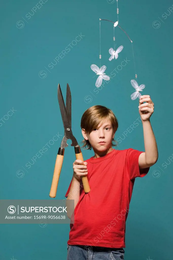 Boy standing below butterfly mobile, holding hedge clippers