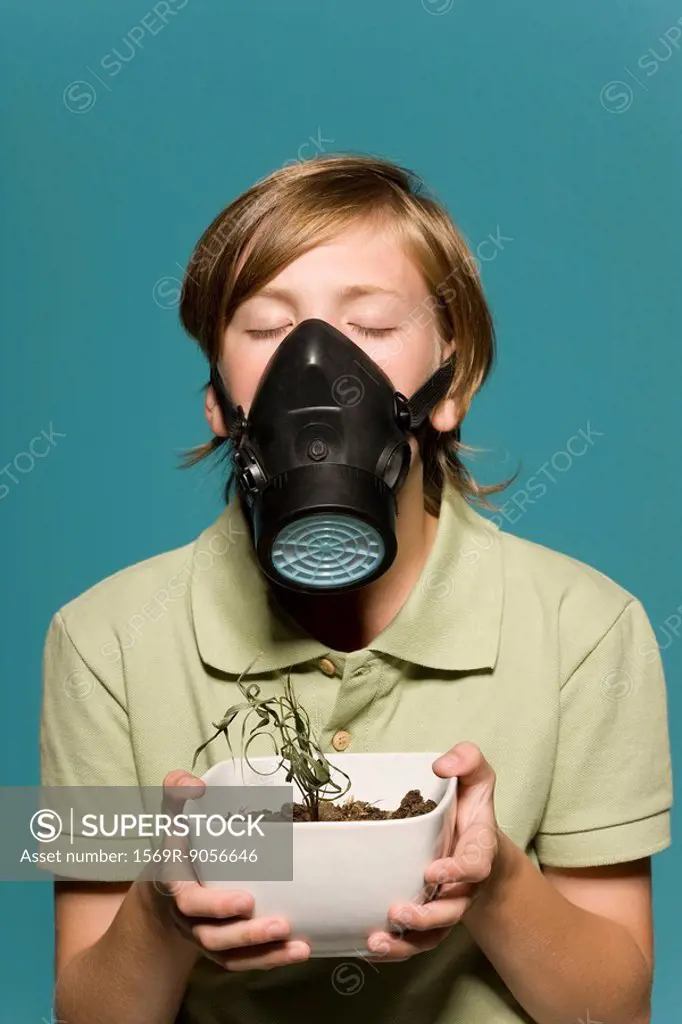 Boy wearing gas mask, holding wilted potted plant