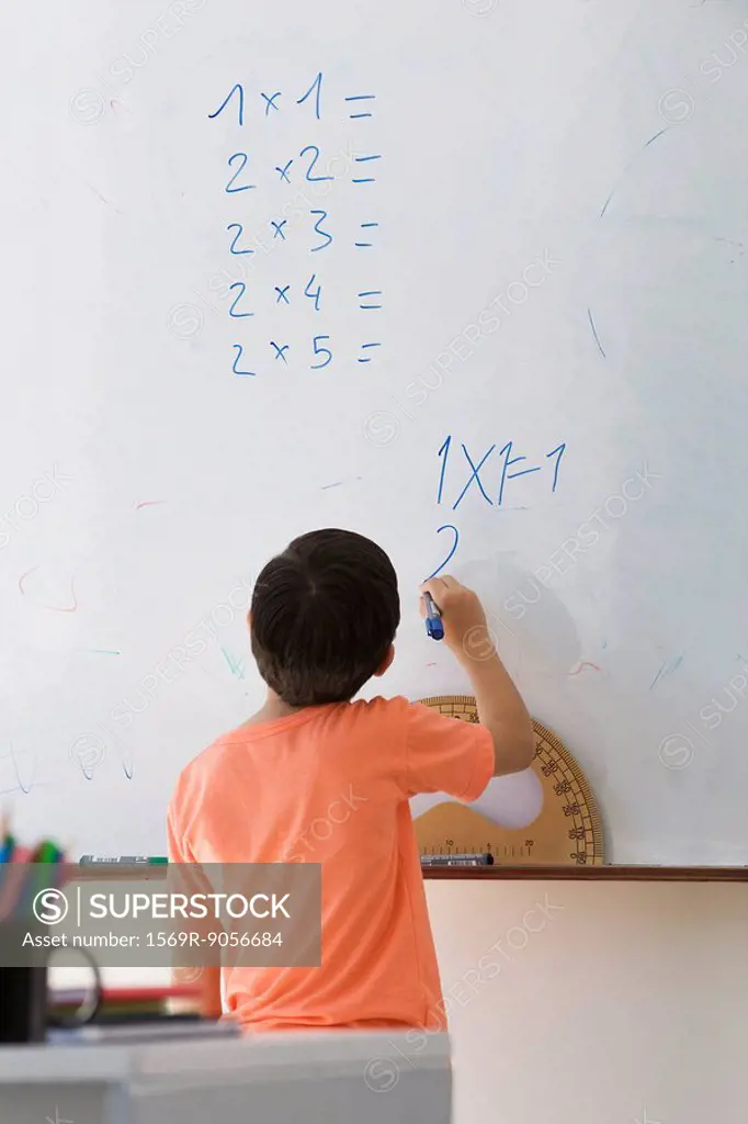 Elementary school student doing math equation on whiteboard, rear view
