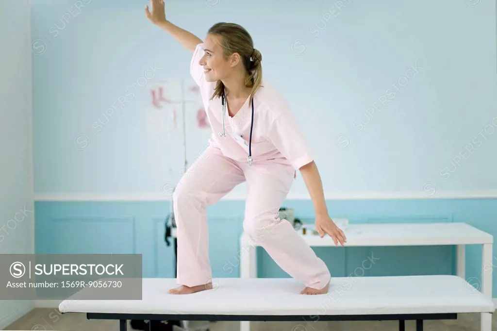 Female medical student standing on top of examination table, pretending to surf