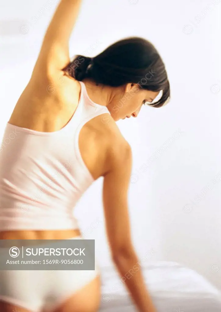 Woman standing in underwear, stretching, rear view