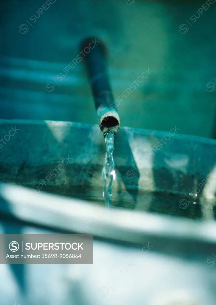 Water trickling from metal pipe into bucket, extreme close-up