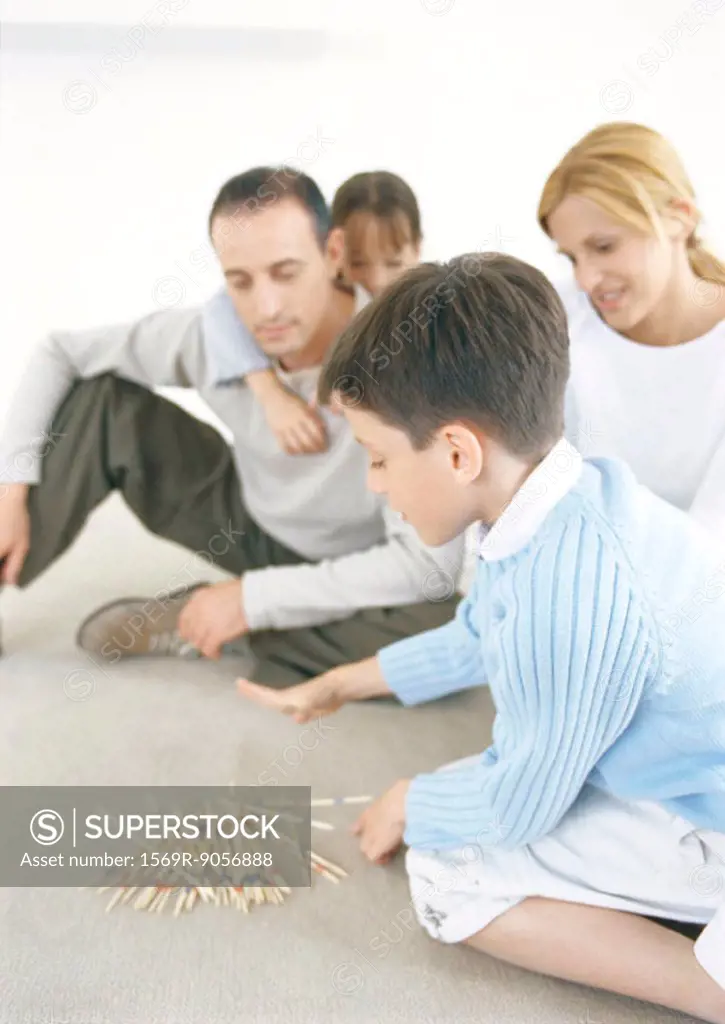 Family playing pick-up-sticks on floor