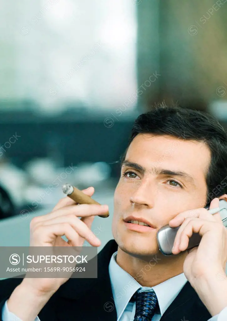 Businessman using cell phone and smoking cigar