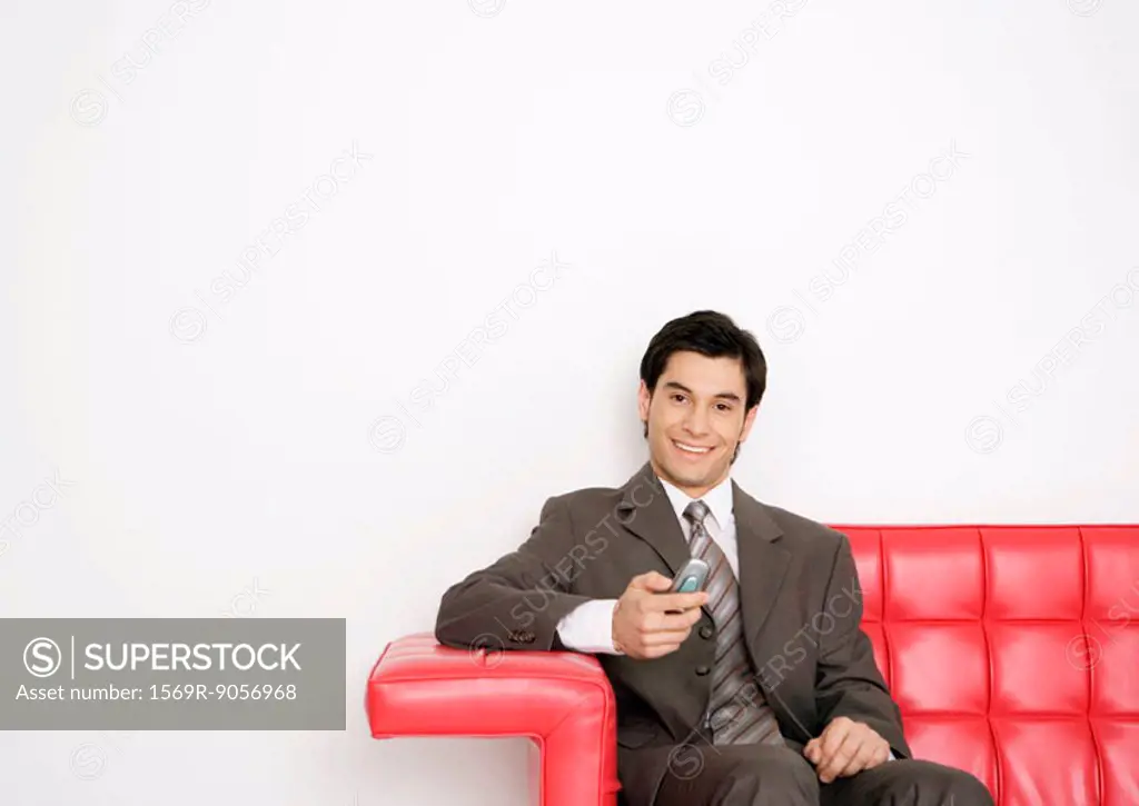 Young businessman sitting on sofa, holding cell phone, and smiling