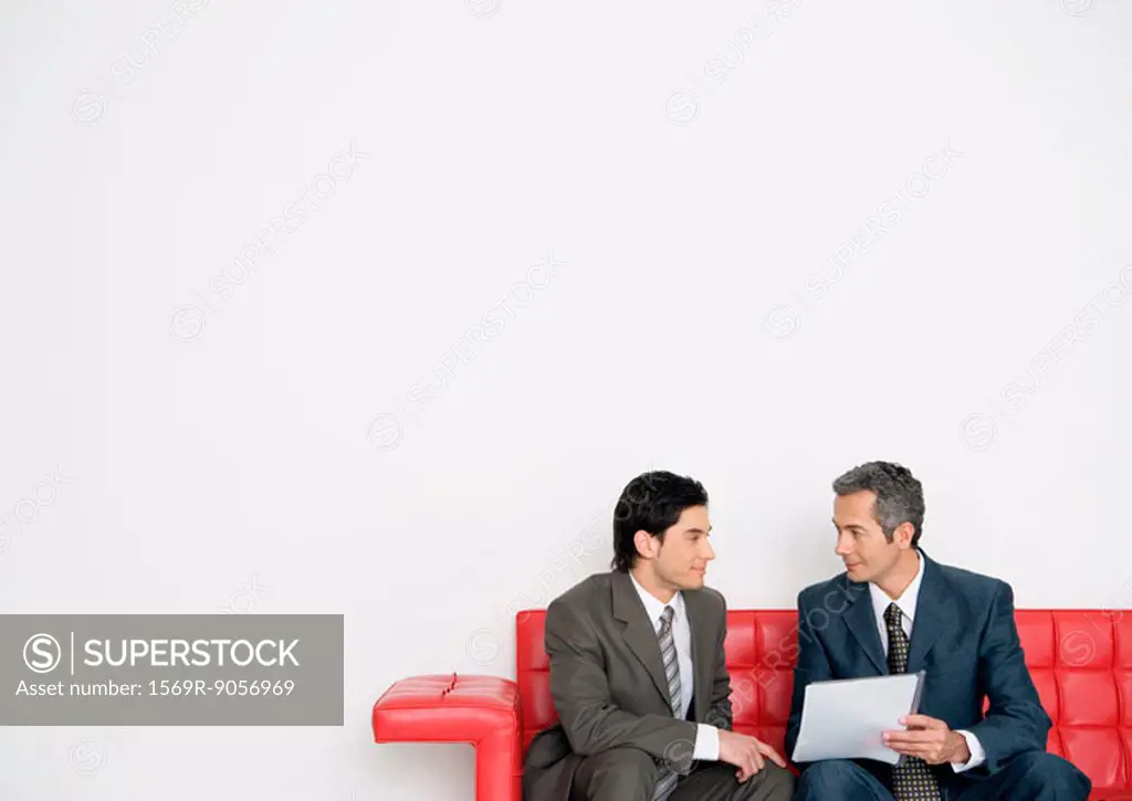 Two businessmen discussing document together on sofa