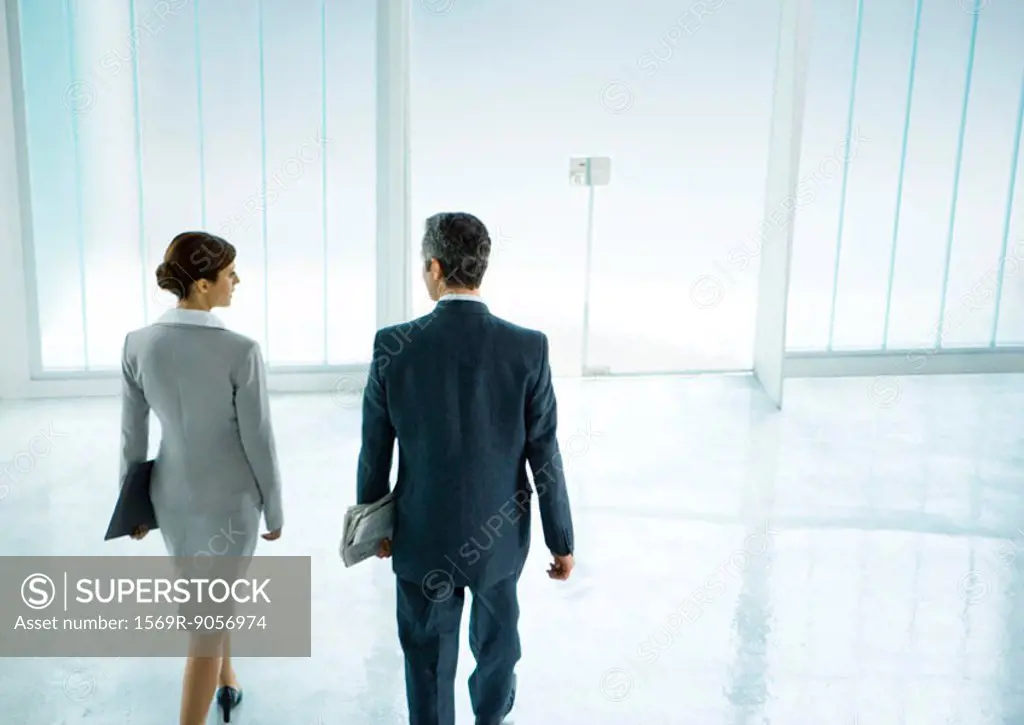 Male and female business partners walking toward door in lobby
