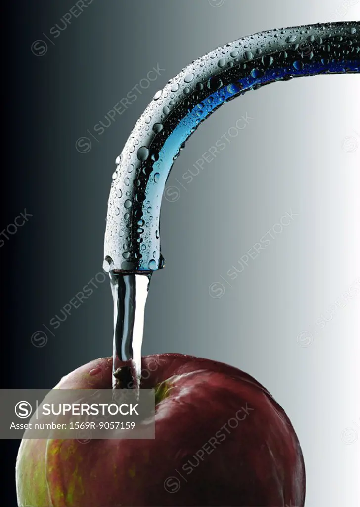 Water running from faucet onto apple, close-up