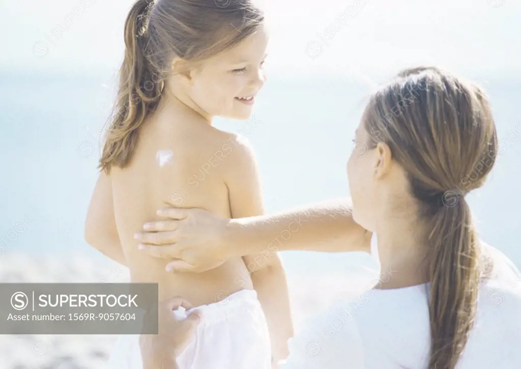 Woman rubbing sunscreen into girl´s back