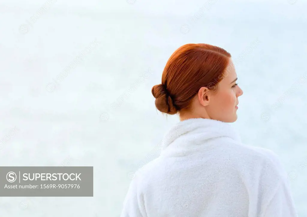 Woman wearing bathrobe, overlooking sea, rear view