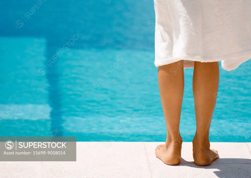 Woman wearing bathrobe standing by side of pool, rear view of legs