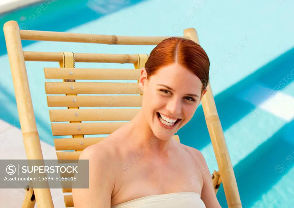 Woman sitting in deckchair smiling, pool in background