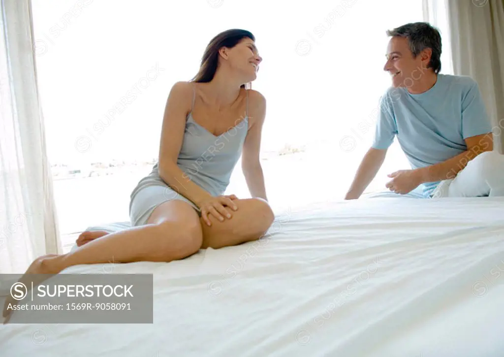 Mature couple sitting on bed, smiling at each other