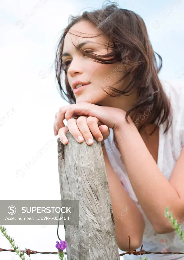 Young woman leaning on wooden post