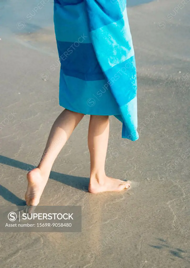 Child wrapped in towel walking on wet sand