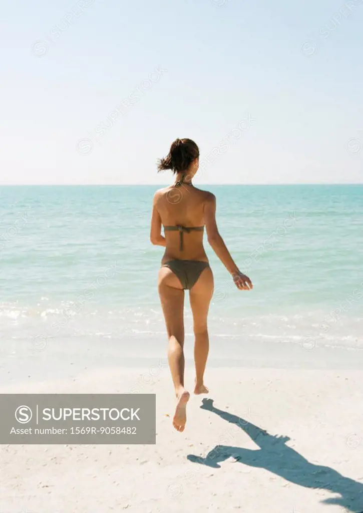 Young woman on beach running toward ocean, rear view