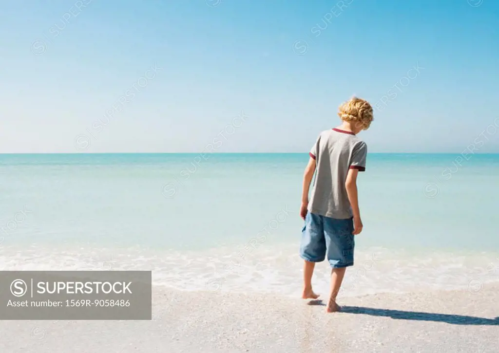 Boy testing water with toe at beach, rear view