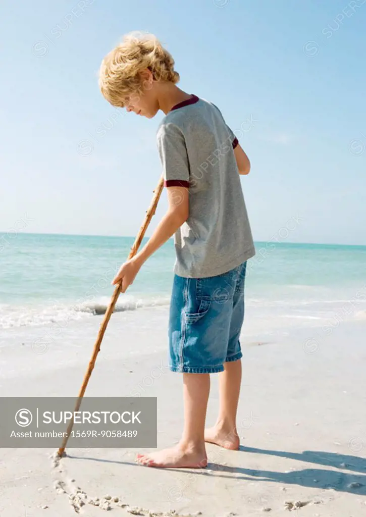 Boy drawing with stick on sand