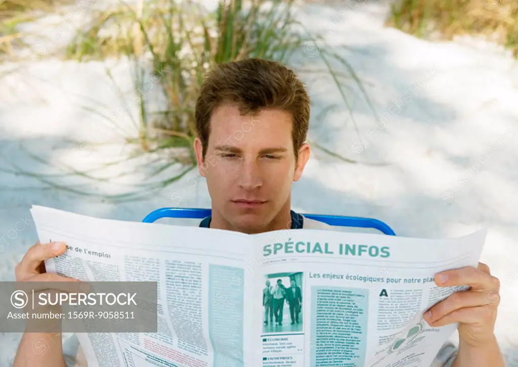 Man reading newspaper on beach