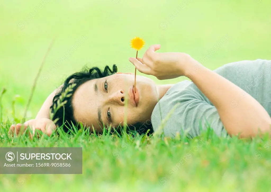 Young woman lying on grass with flower in mouth