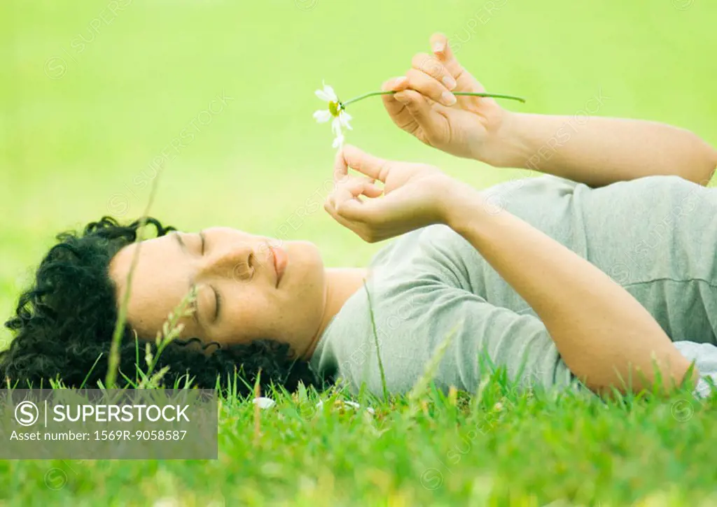 Young woman lying on grass plucking petals from flower