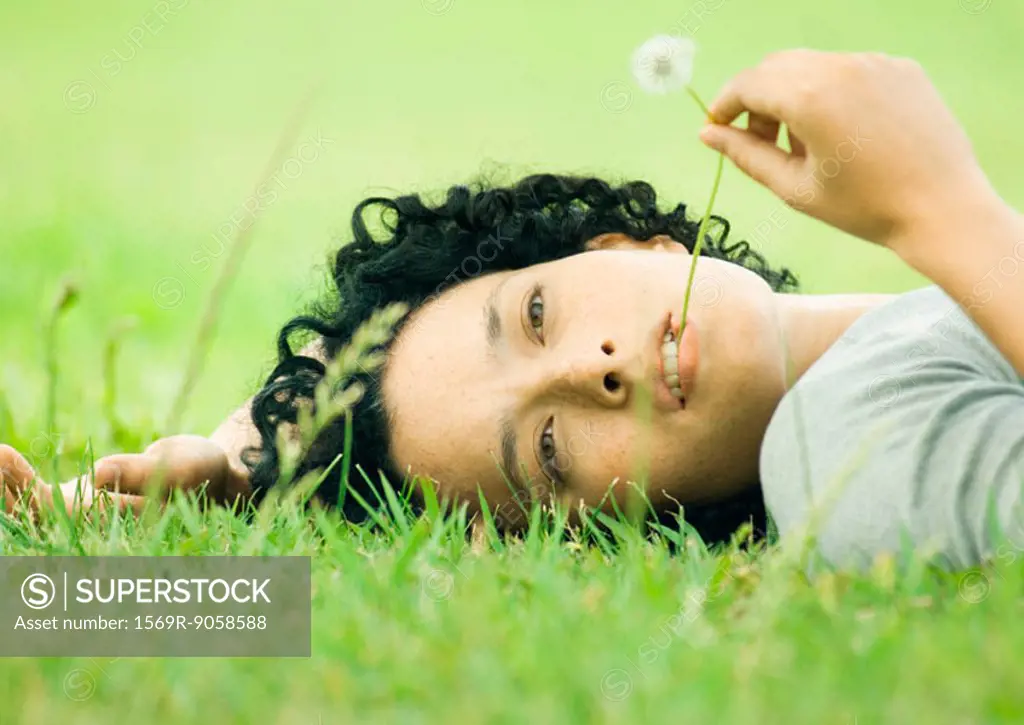 Young woman lying on grass with dandelion stem in mouth