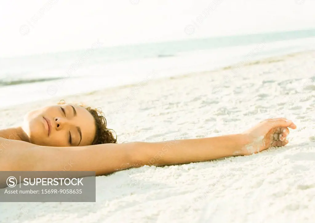 Woman lying on sand, view of head and arm