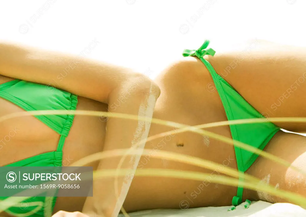 Woman lying on beach in bikini, mid section