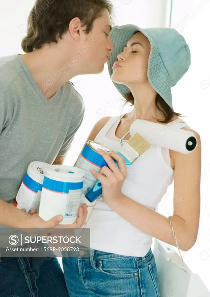 Couple holding painting supplies and kissing