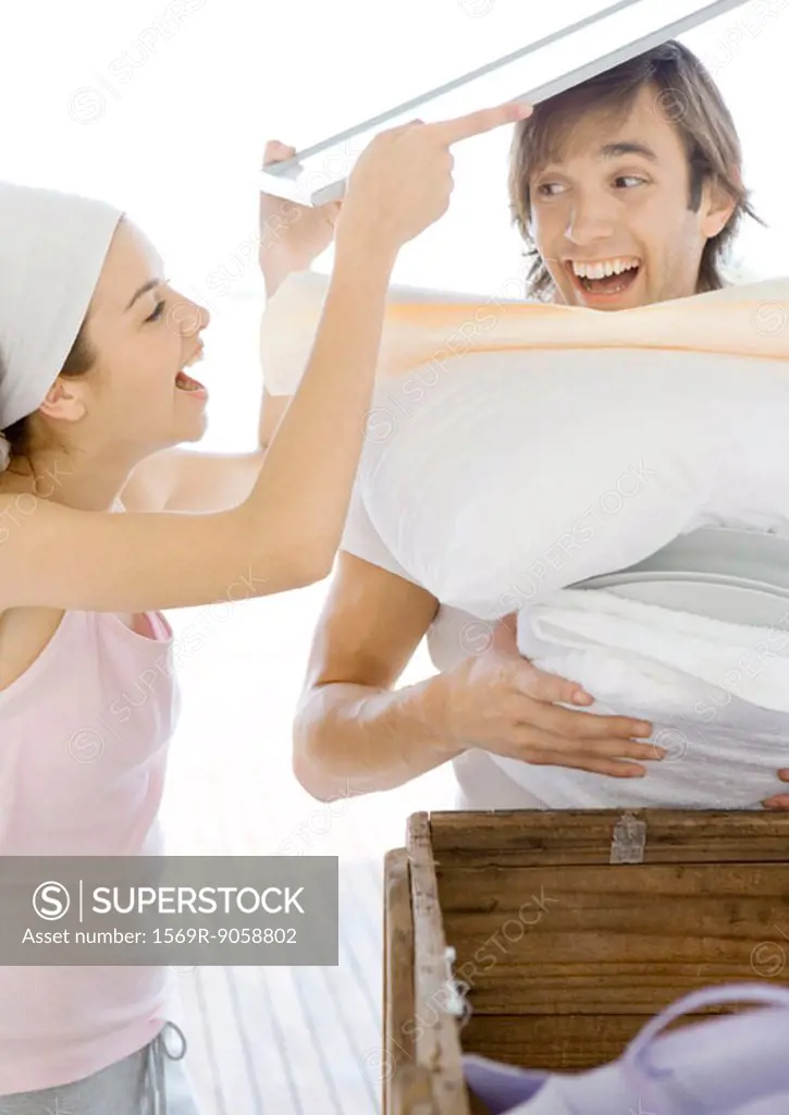 Woman stacking household objects onto man, laughing