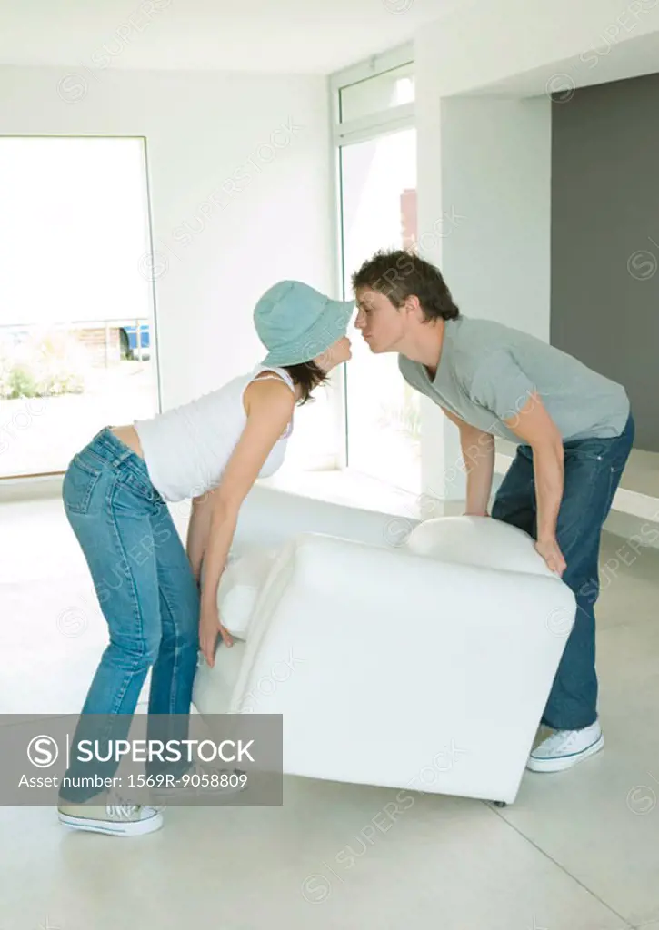Couple kissing as they move armchair together