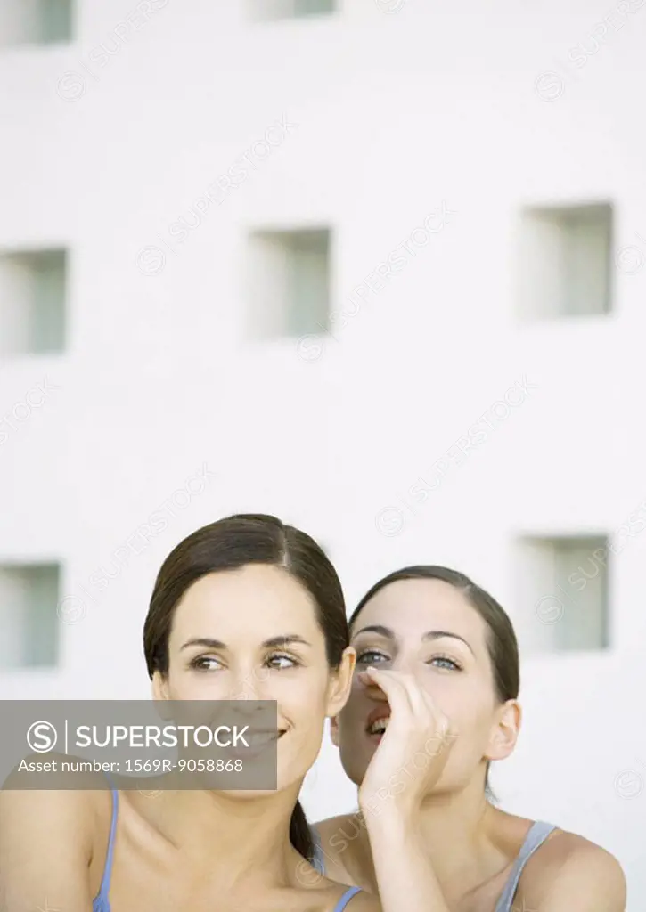 Young woman whispering to friend