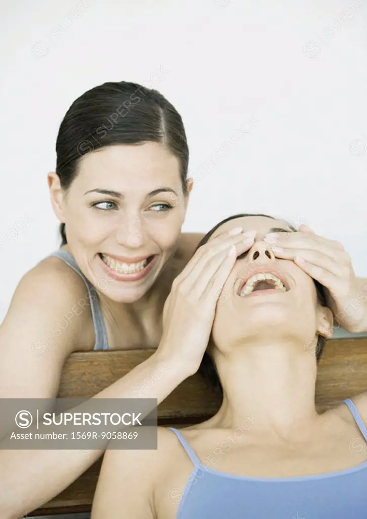 Young woman covering her friend´s eyes, both smiling, portrait