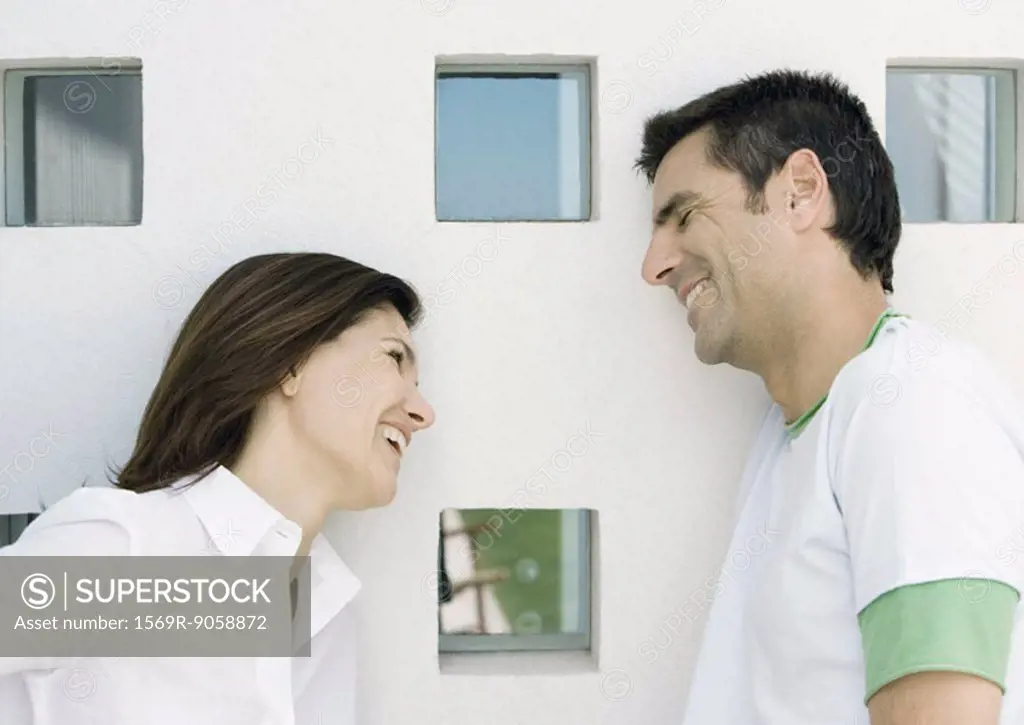 Woman and husband, both leaning against wall with squared windows and smilling