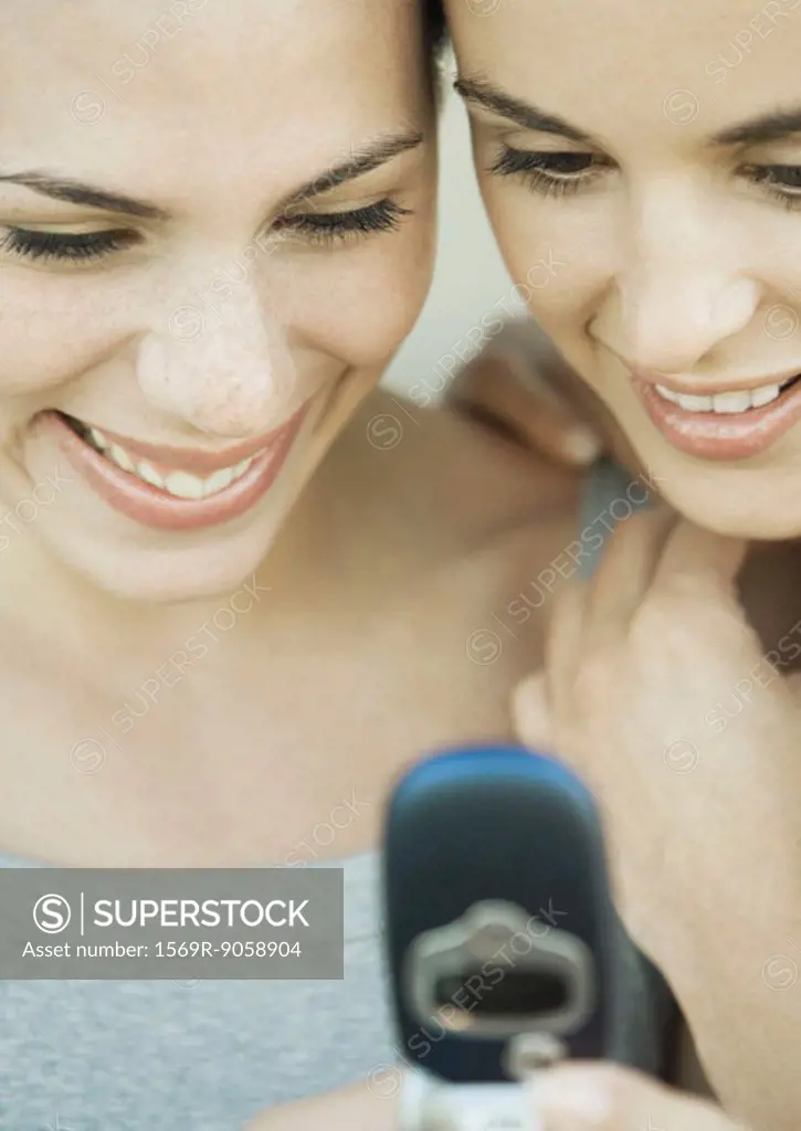 Two young women side by side looking down at a cell phone, both smiling, extreme close-up