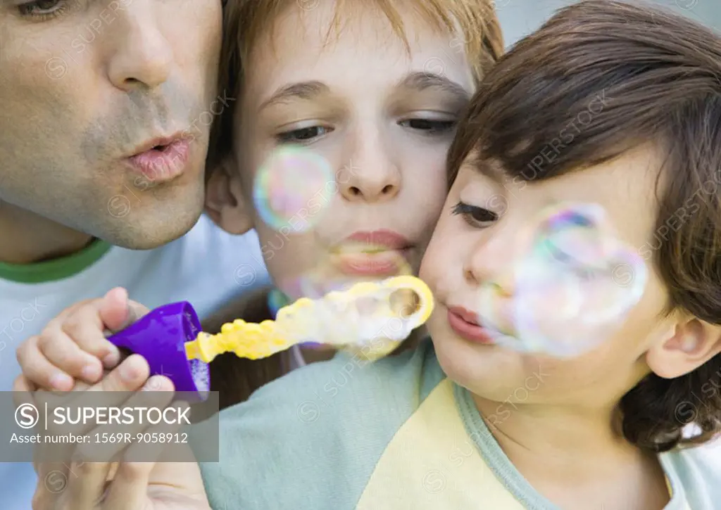 Father having fun with his two chiildren, blowing soap bubbles together, portrait, extreme close-up