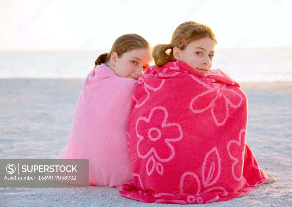 Two girls sitting wrapped in towels on beach