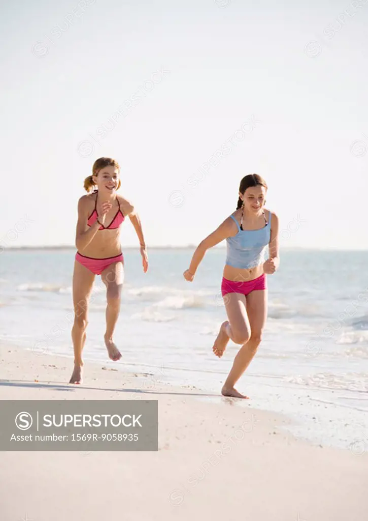 Two preteen girls running on beach