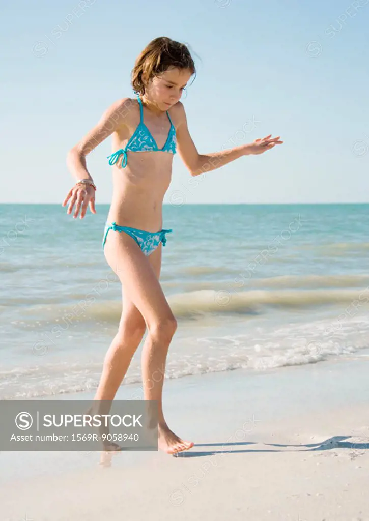 Girl on beach, walking away from water on tiptoes