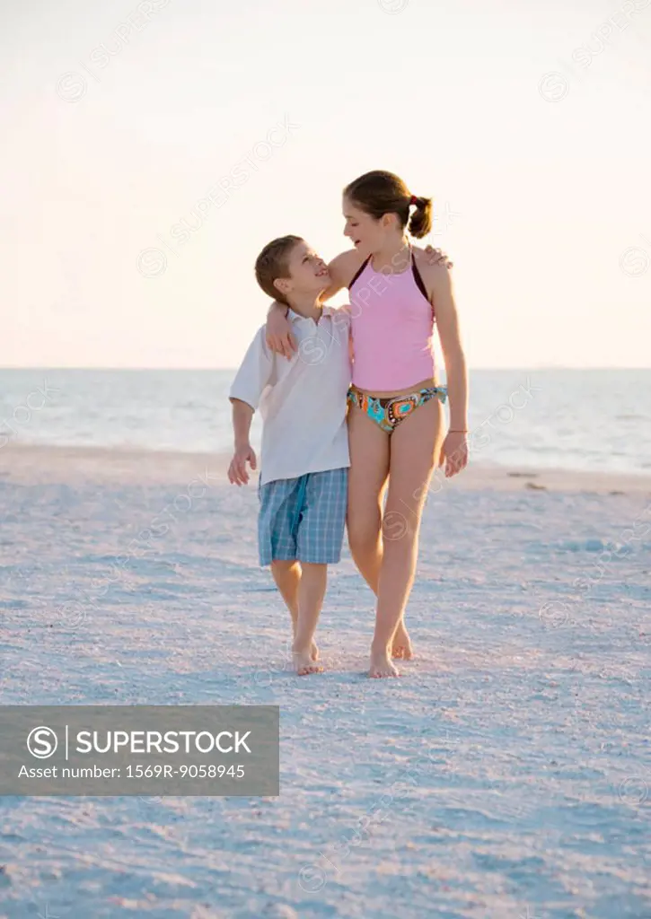 Girl and boy walking with arms around each other´s shoulder´s on beach