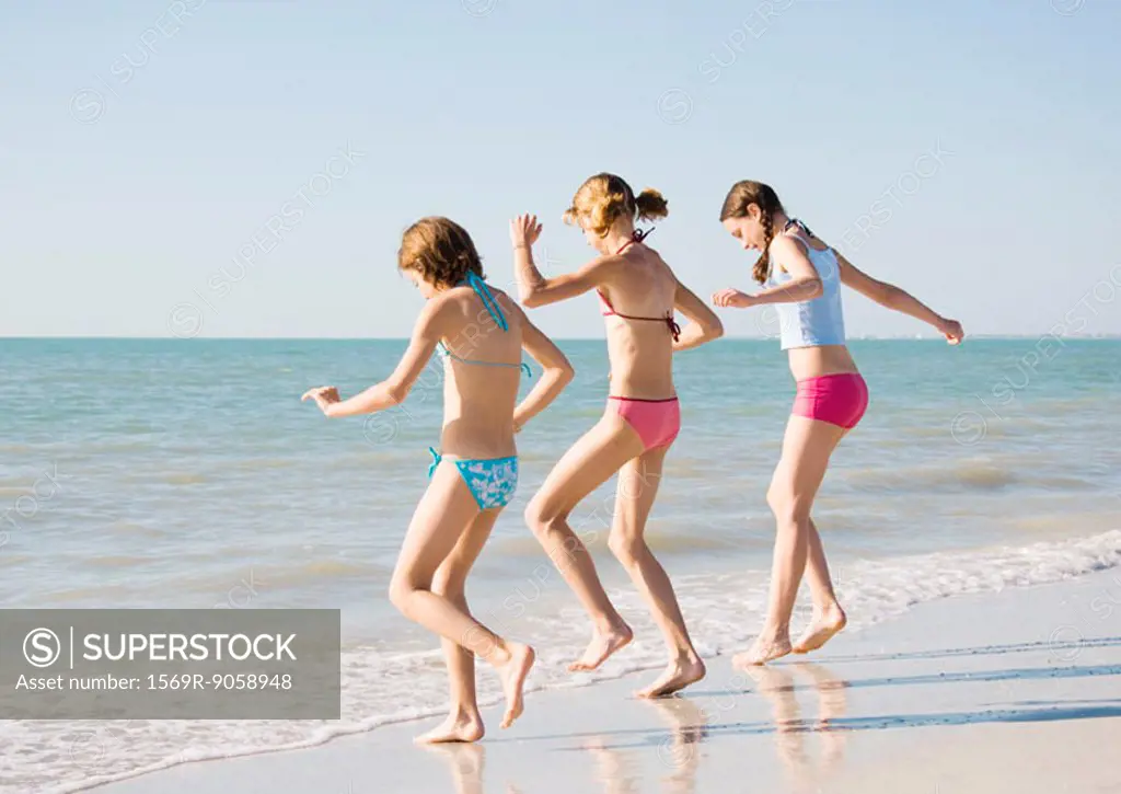 Three girls running toward water on beach