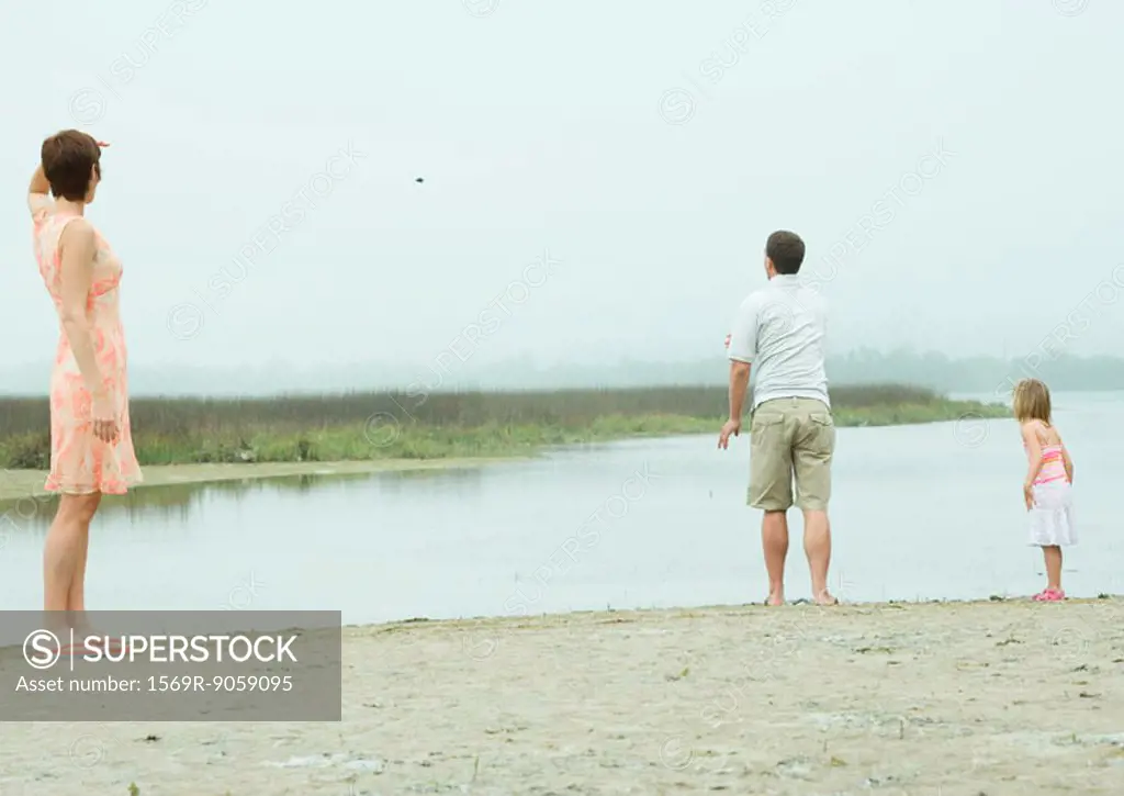 Man throwing pebble into water while family watches