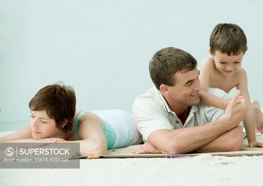Family lying on beach, man and son thumb wrestling while mother sleeps