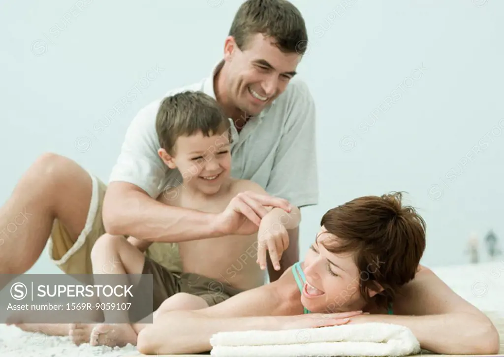 Family on beach, man and son bothering woman while she´s lying down