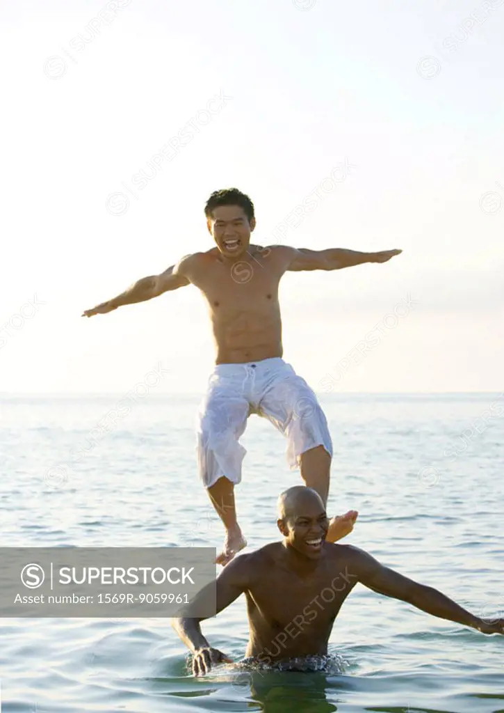 In sea, man standing on second man´s shoulders is losing balance